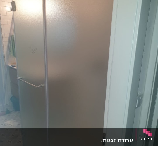 דלת זכוכית חלבית עם ידית מתכת בחדר אמבטיה